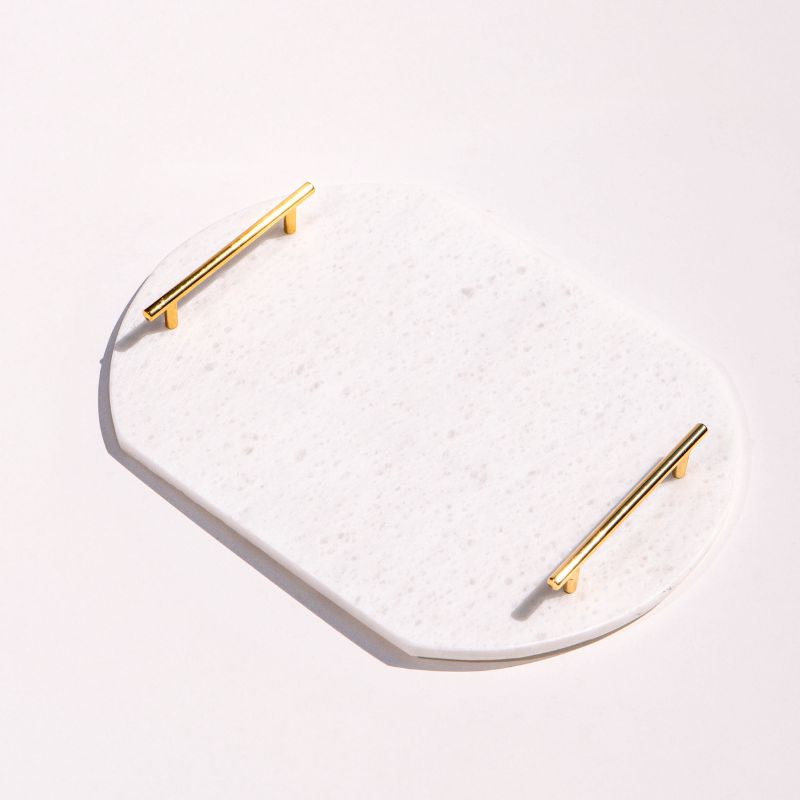 White oval capsule-shaped marble tray with brass handles placed by the pool