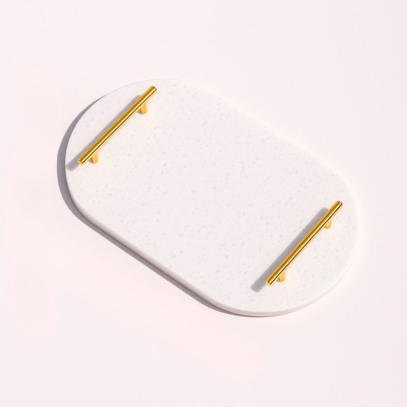 White oval capsule-shaped marble tray with brass handles placed by the pool