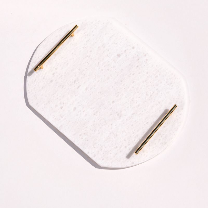 White oval capsule-shaped marble tray with brass handles placed by the pool