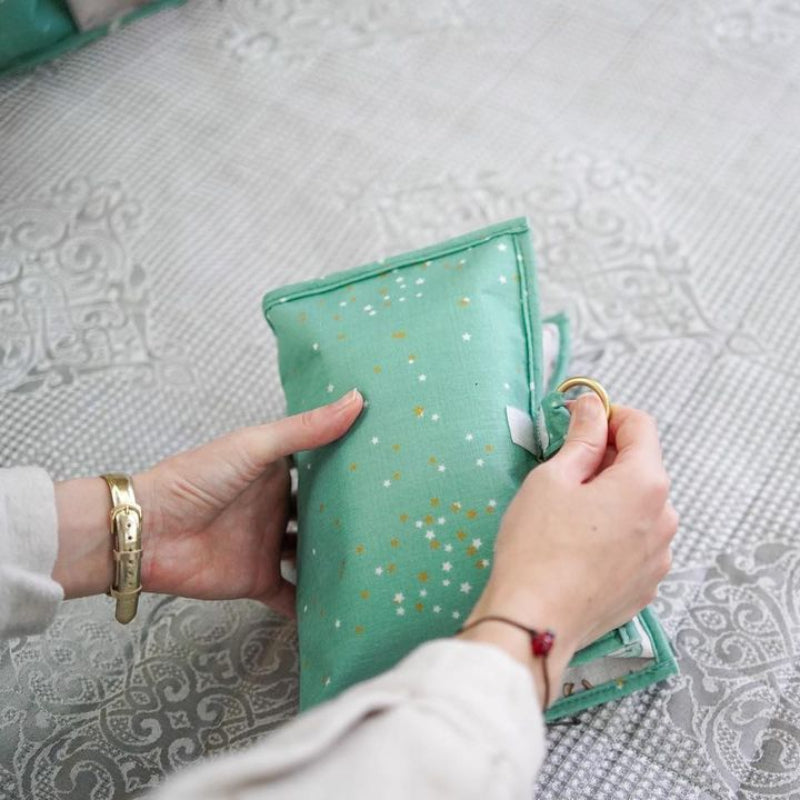 Foldable baby changing mat with built-in storage pockets and diapers, shown above a baby lying on a soft mat