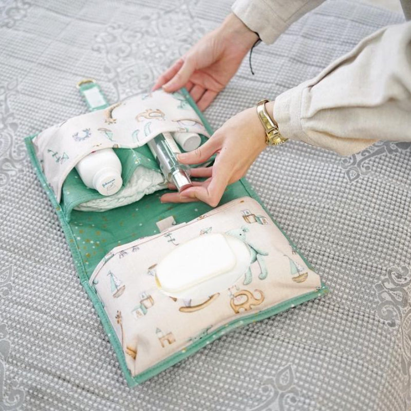 Foldable baby changing mat with built-in storage pockets and diapers, shown above a baby lying on a soft mat
