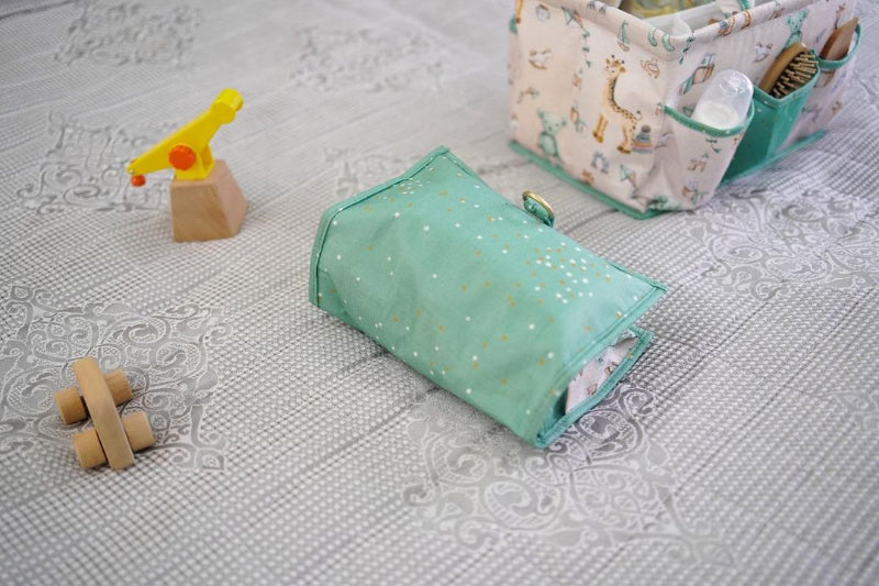 Foldable baby changing mat with built-in storage pockets and diapers, shown above a baby lying on a soft mat