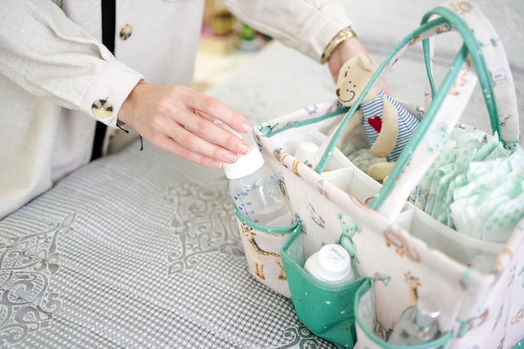 Portable baby diaper caddy organizer with compartments, filled with bottles, wipes, diapers, and teddy bear