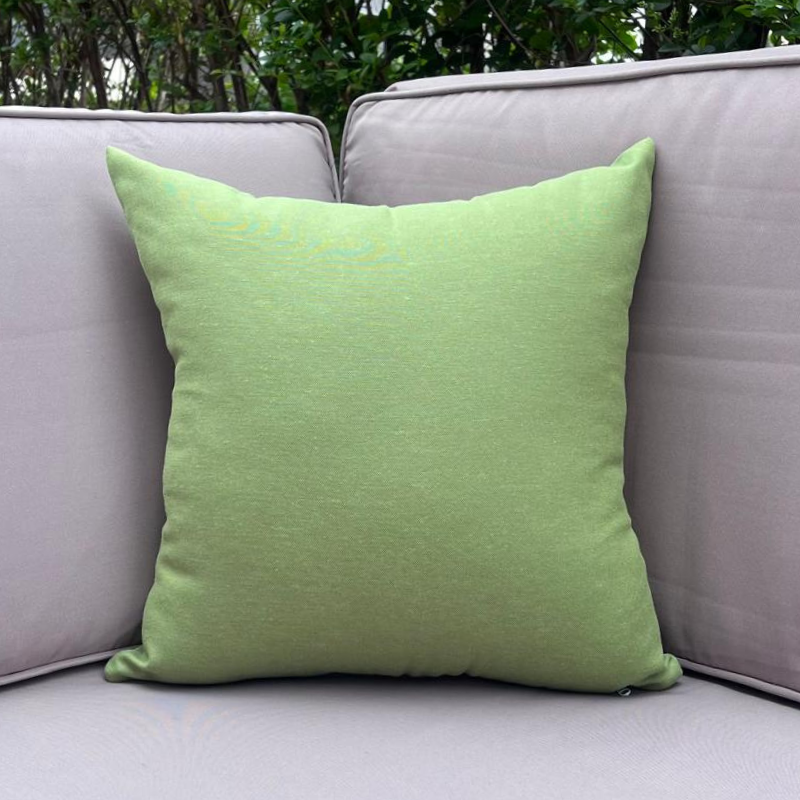 Plain green cushion cover displayed on an outdoor beige sofa in a garden setting