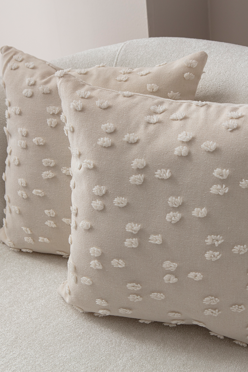 Beige textured cushion with raised knot-dot details displayed on a light curved sofa.