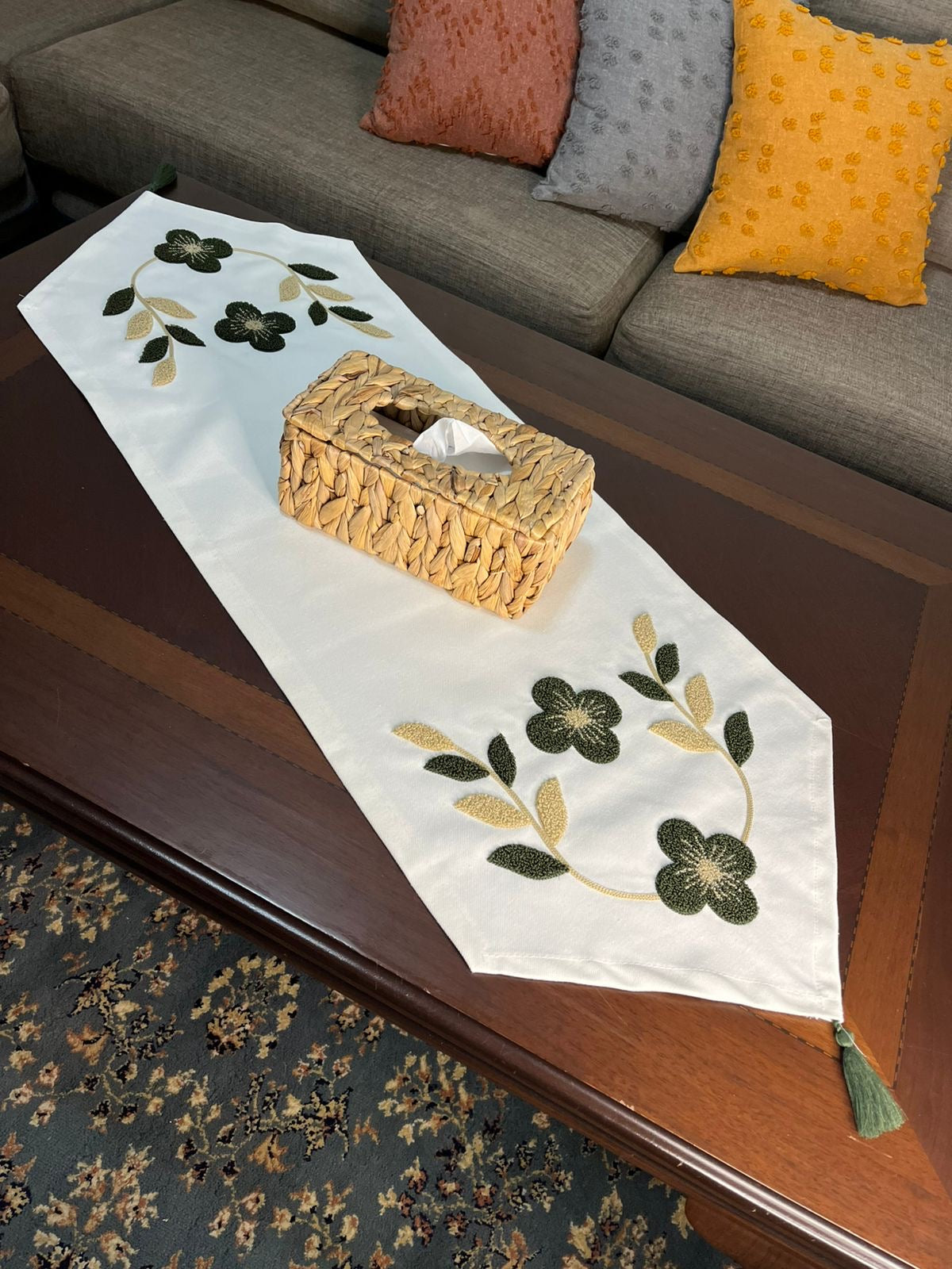 White embroidered table runner with green and gold floral design on wooden coffee table