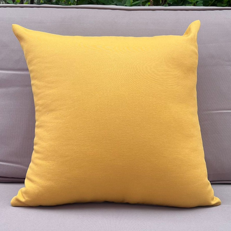 Mustard yellow cushion cover displayed on a beige outdoor sofa in a garden patio setting