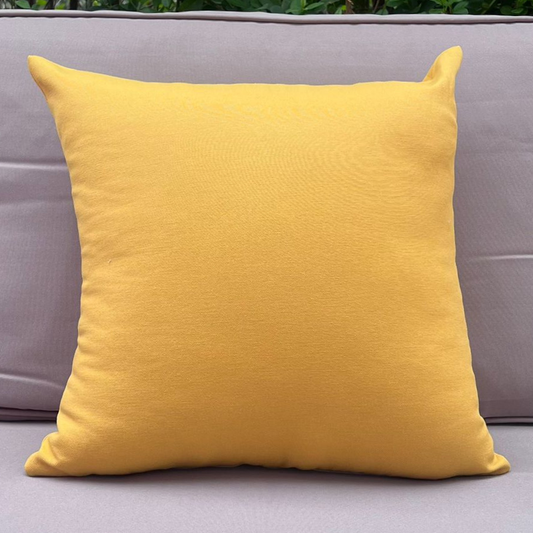 Mustard yellow cushion cover displayed on a beige outdoor sofa in a garden patio setting