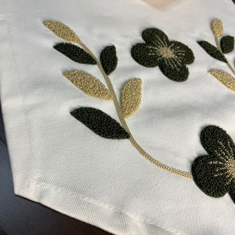 White embroidered table runner with green and gold floral design on wooden coffee table