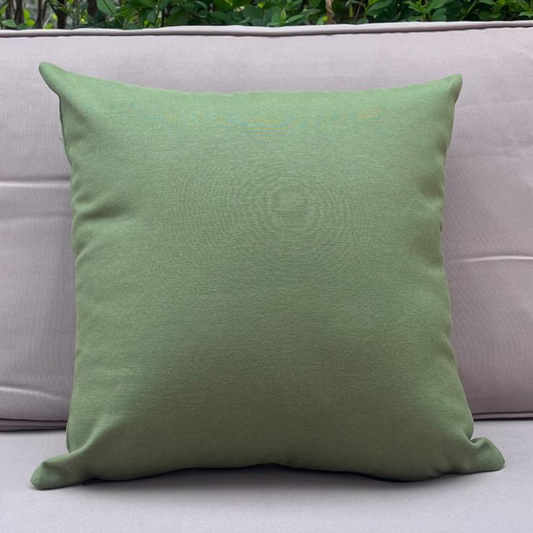 Sage green cushion cover displayed on a beige outdoor sofa in a garden patio setting