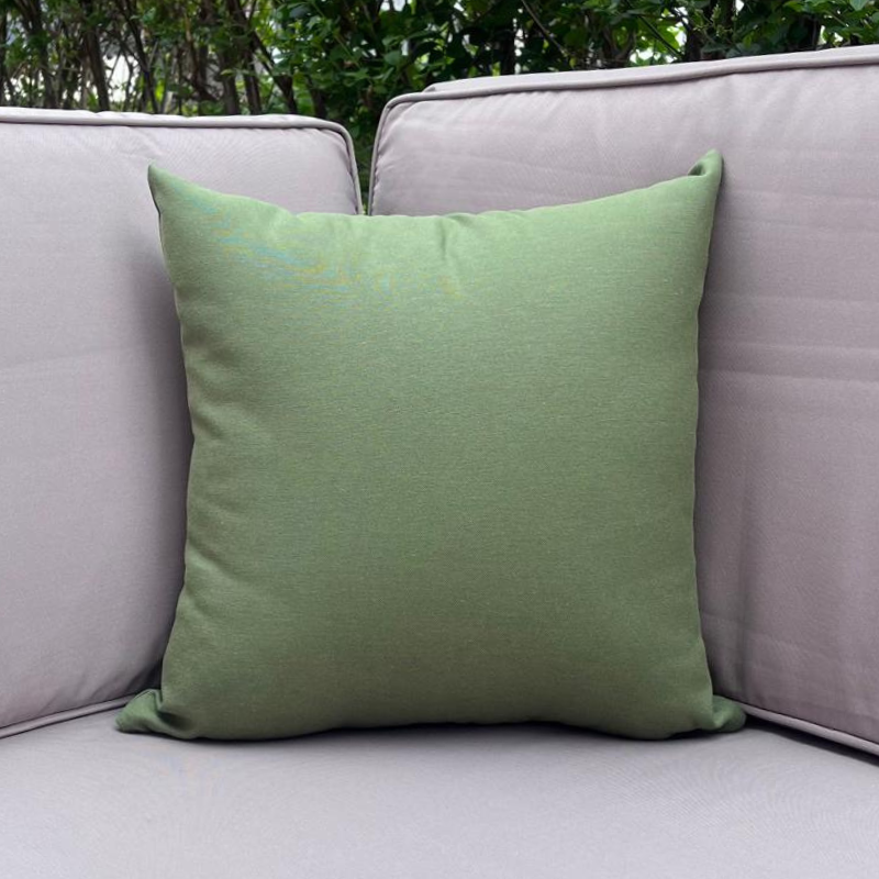 Sage green cushion cover displayed on a beige outdoor sofa in a garden patio setting
