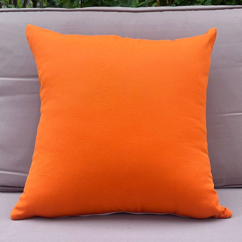 Orange pillow on a gray sofa with greenery in the background