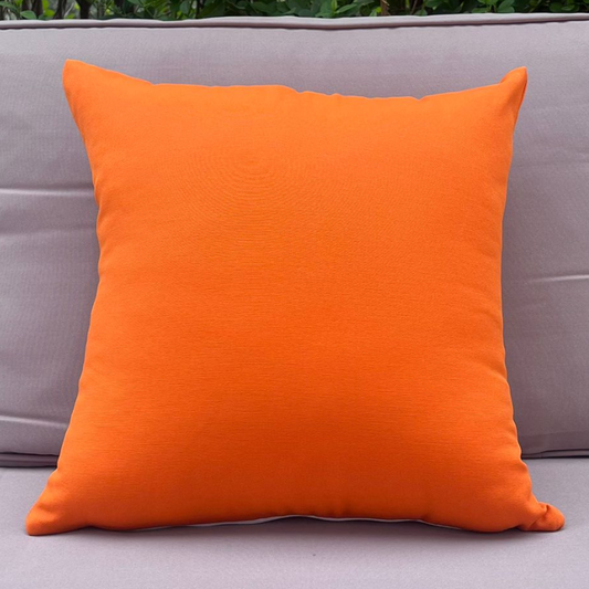 Orange pillow on a gray sofa with greenery in the background