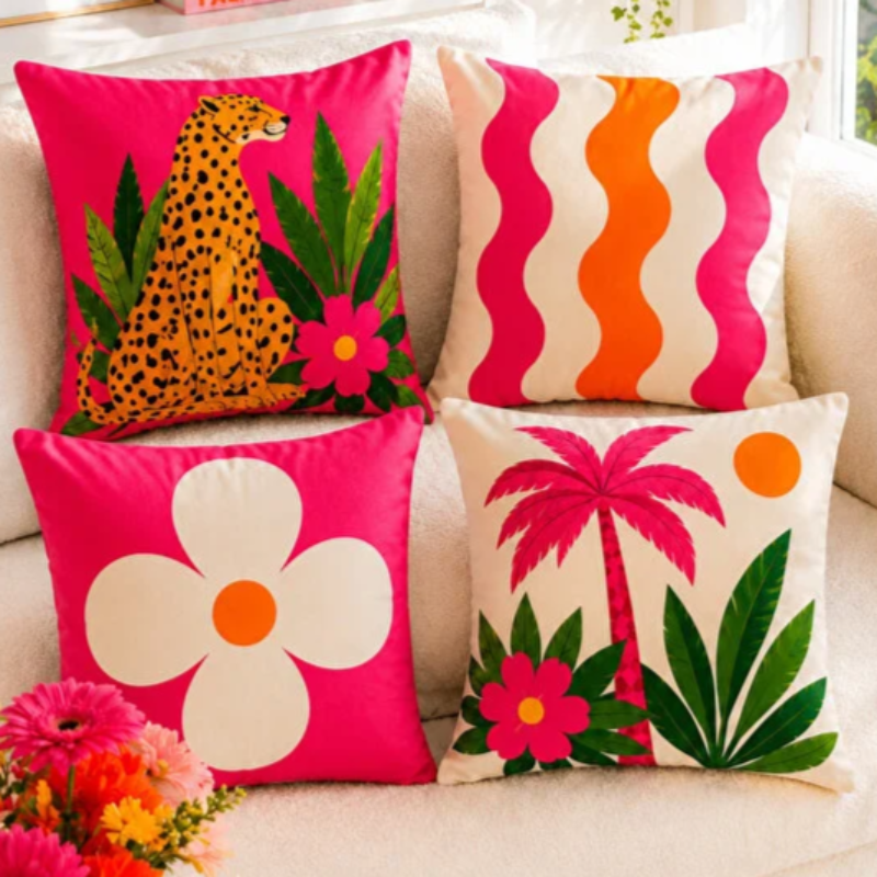 Set of four vibrant tropical decorative cushion covers featuring a cheetah illustration, abstract coral waves, bold white floral artwork, and a palm tree design displayed on a modern white sofa in a lush garden setting.