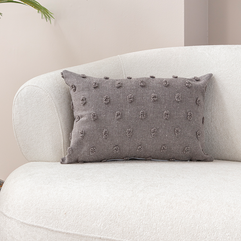 Taupe textured cushion with raised knot-dot details placed on a light beige curved sofa.