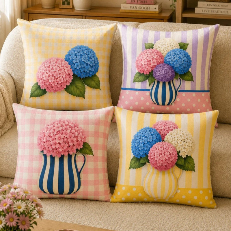 Set of four pastel hydrangea decorative cushion covers featuring floral bouquets, striped ceramic vases, gingham backgrounds, and soft yellow, pink, lavender, and blue accents displayed on a cozy armchair.