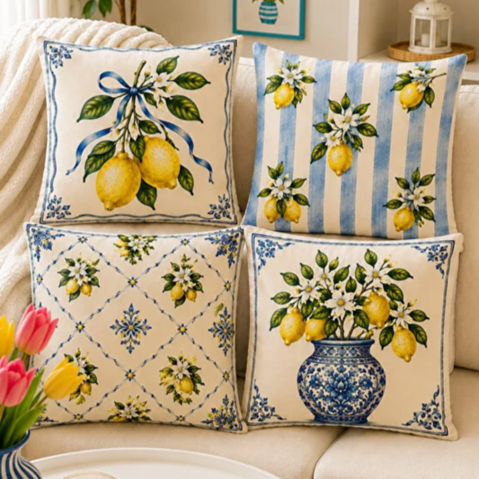 Set of four Mediterranean-inspired decorative cushion covers featuring lemons, citrus blossoms, blue ceramic vases, striped patterns, and traditional Italian tile motifs displayed on a neutral sofa.