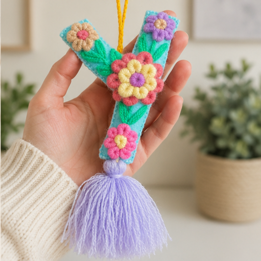 Handmade embroidered letter Y ornament with colorful floral embroidery and lavender tassel on wooden background