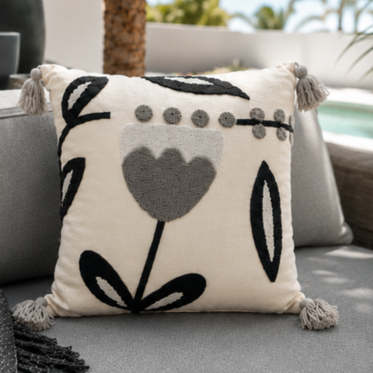 Embroidered floral cushion with navy and grey design, soft cream fabric, and tassel accents on each corner, perfect for home decor."