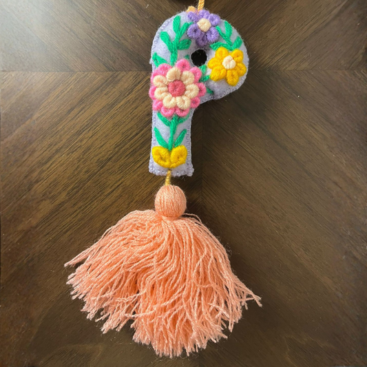 Handmade embroidered letter P ornament with floral patterns and peach tassel on wooden background