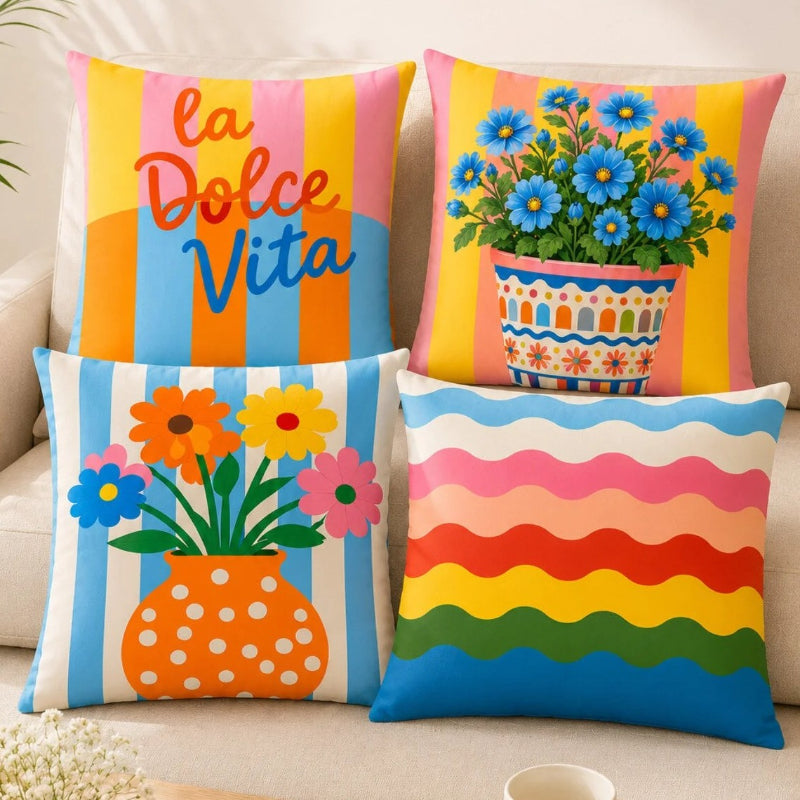 Set of four colorful Mediterranean-inspired decorative cushion covers featuring "La Dolce Vita" typography, floral ceramic planters, striped backgrounds, and a vibrant rainbow wave pattern displayed on a modern cream sofa.
