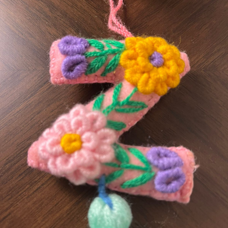 Handmade embroidered letter Z ornament with colorful floral stitching and light green tassel on wooden background