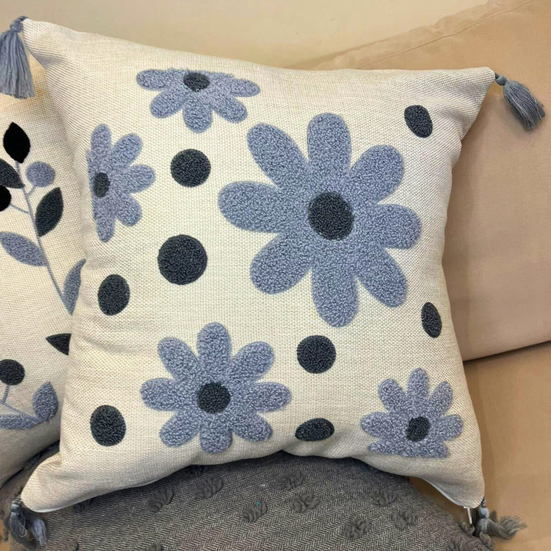 Square embroidered blue daisy cushion cover with tassels on beige sofa