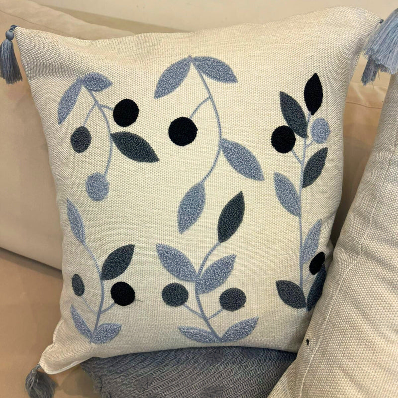 Square embroidered blue botanical cushion cover with tassels on beige sofa