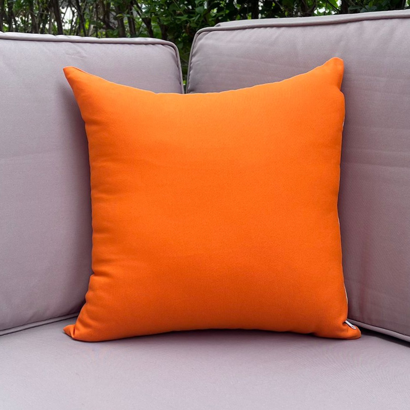 Orange pillow on a gray outdoor sofa with greenery in the background