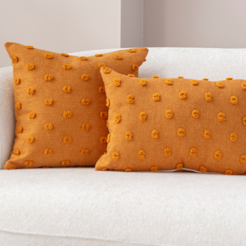 Mustard yellow textured cushion with raised knot-dot details placed on a light beige curved sofa.