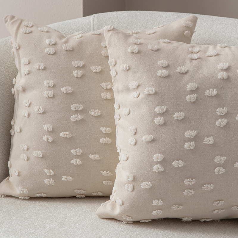 Beige textured cushion with raised knot-dot details displayed on a light curved sofa.