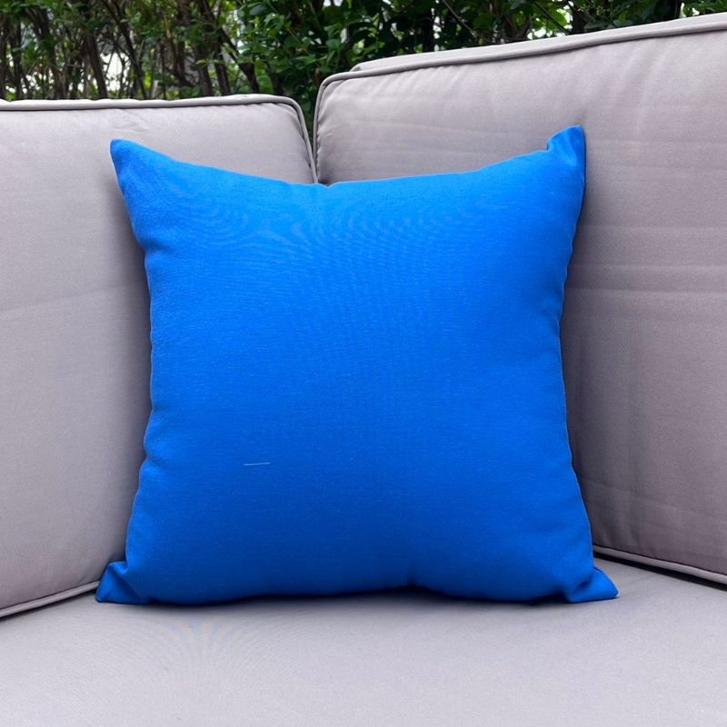 Royal blue cushion cover displayed on a beige outdoor sofa in a garden patio setting
