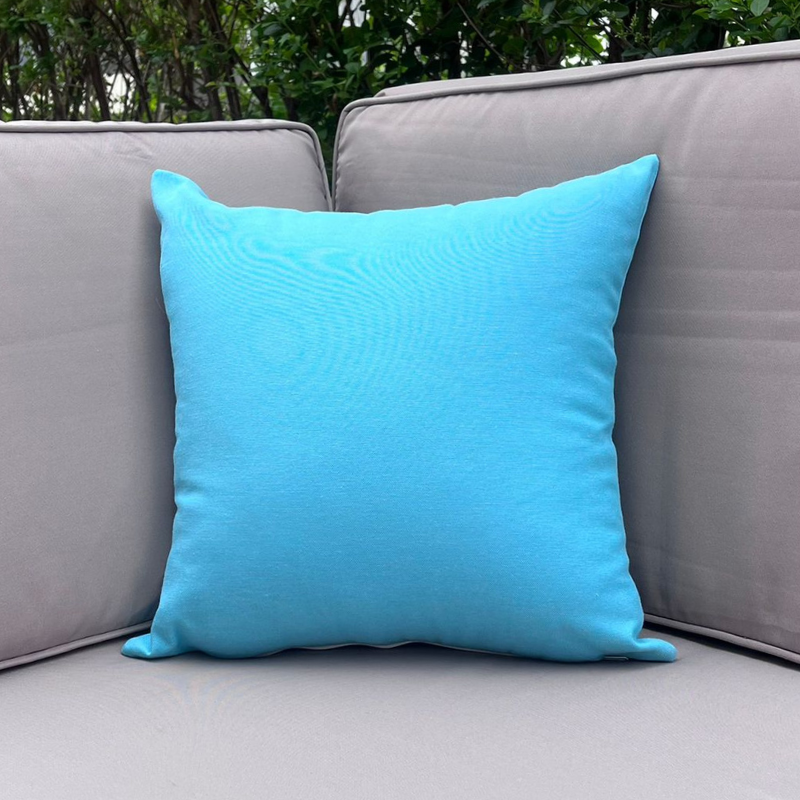 Turquoise cushion cover displayed on a beige outdoor sofa in a garden patio setting