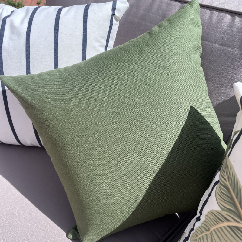 Sage green cushion cover displayed on a beige outdoor sofa in a garden patio setting