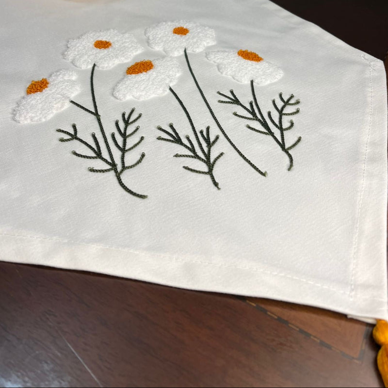 White cotton table runner with embroidered wildflowers and orange centers on wooden coffee table