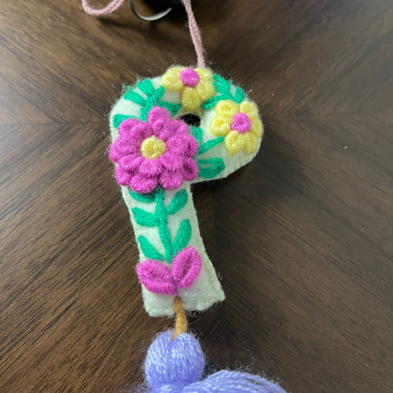 Handmade embroidered letter P ornament with colorful floral embroidery and lavender tassel on wooden background