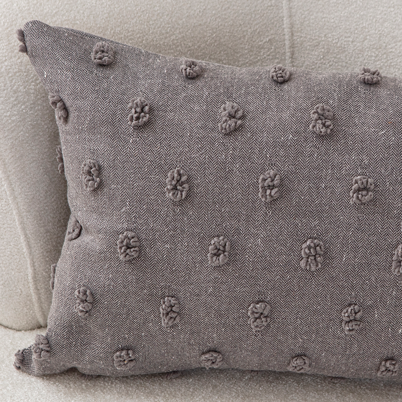 Taupe textured cushion with raised knot-dot details placed on a light beige curved sofa.