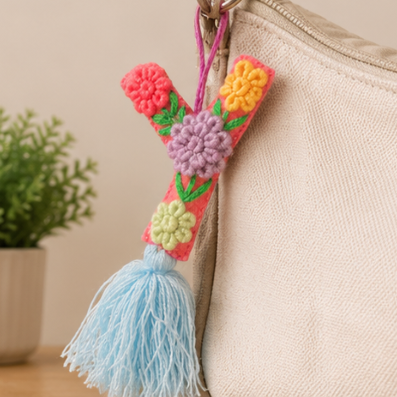 Handmade embroidered letter Y ornament with colorful floral stitching and blue tassel on wooden 