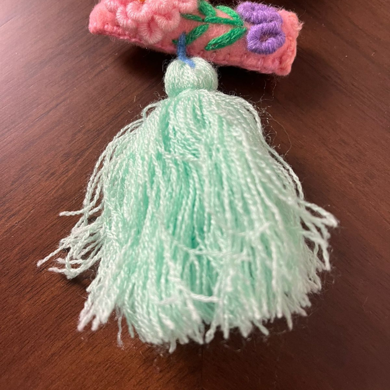 Handmade embroidered letter Z ornament with colorful floral stitching and light green tassel on wooden background
