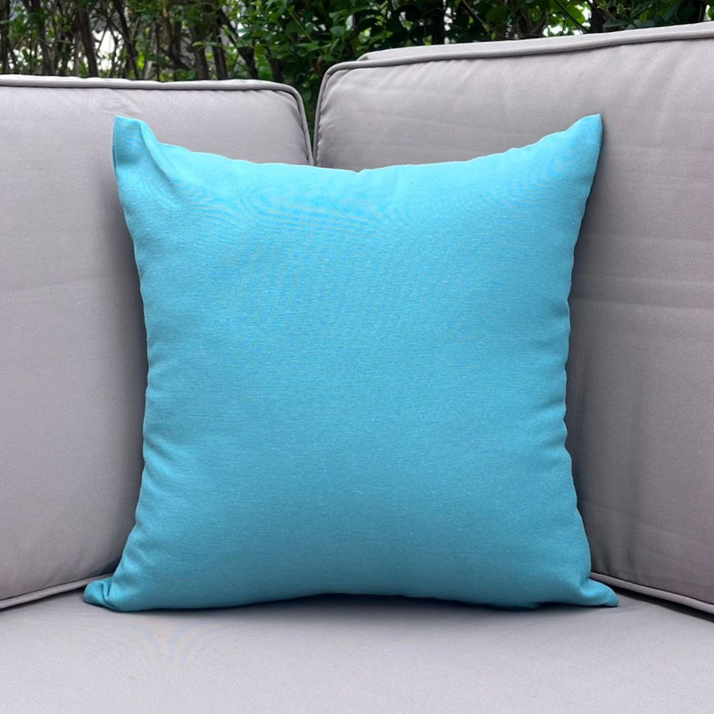 Aqua blue cushion cover displayed on a beige outdoor sofa in a garden patio setting