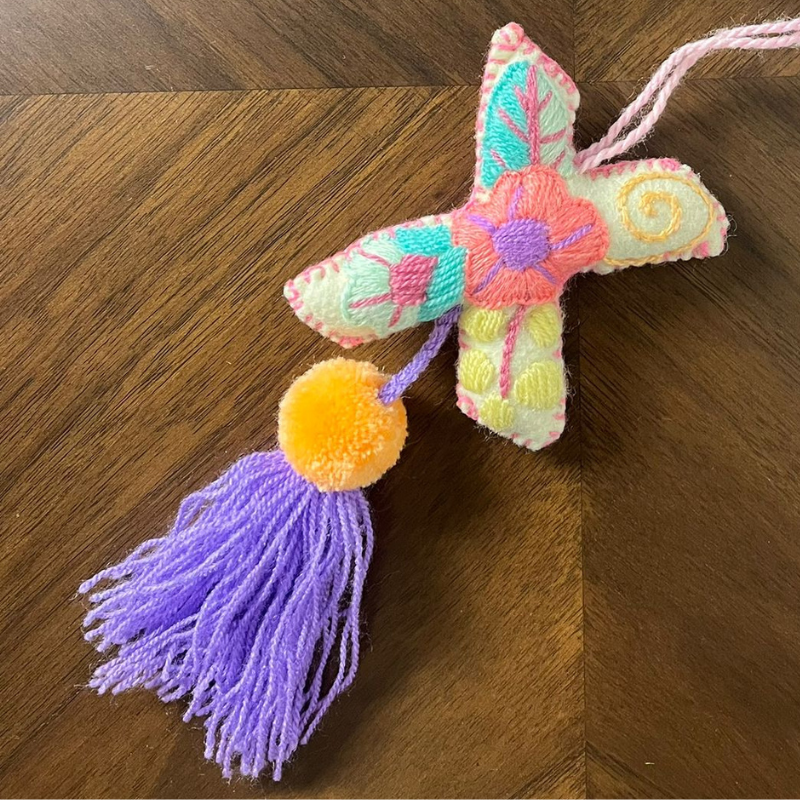 Colorful handmade embroidered letter X ornament with floral patterns, yellow pom pom and purple tassel on wooden background