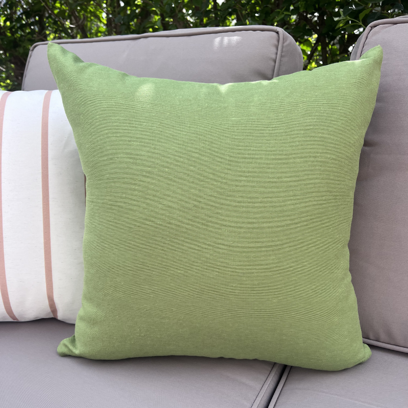Plain green cushion cover displayed on an outdoor beige sofa in a garden setting