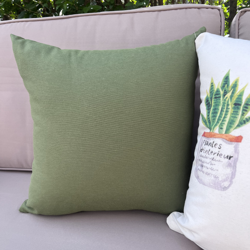 Sage green cushion cover displayed on a beige outdoor sofa in a garden patio setting