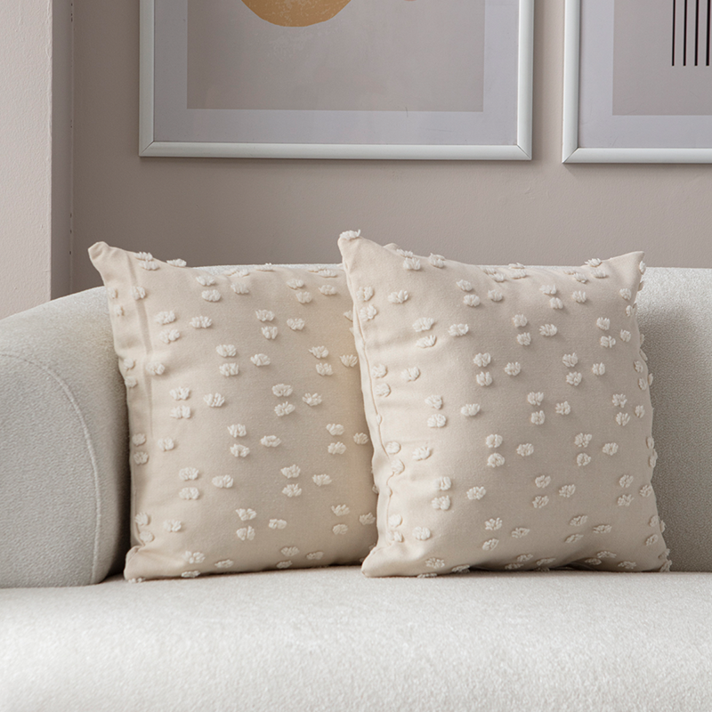 Beige textured cushion with raised knot-dot details displayed on a light curved sofa.
