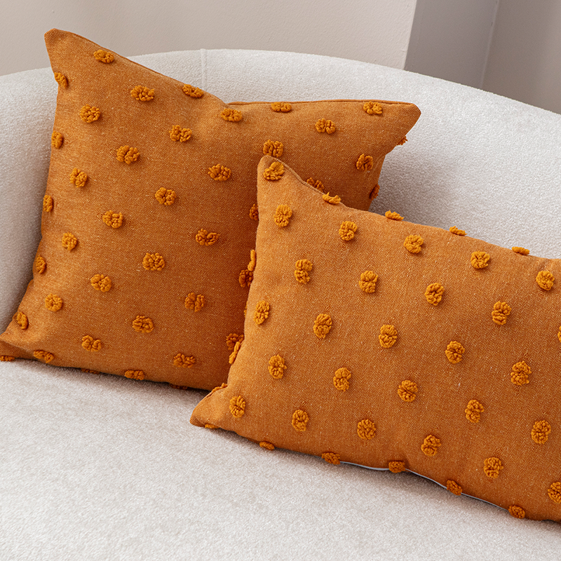 Mustard yellow textured cushion with raised knot-dot details placed on a light beige curved sofa.