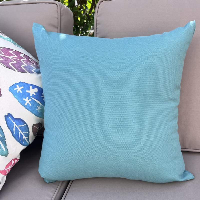 Light blue cushion cover displayed on a beige outdoor sofa in a garden patio setting