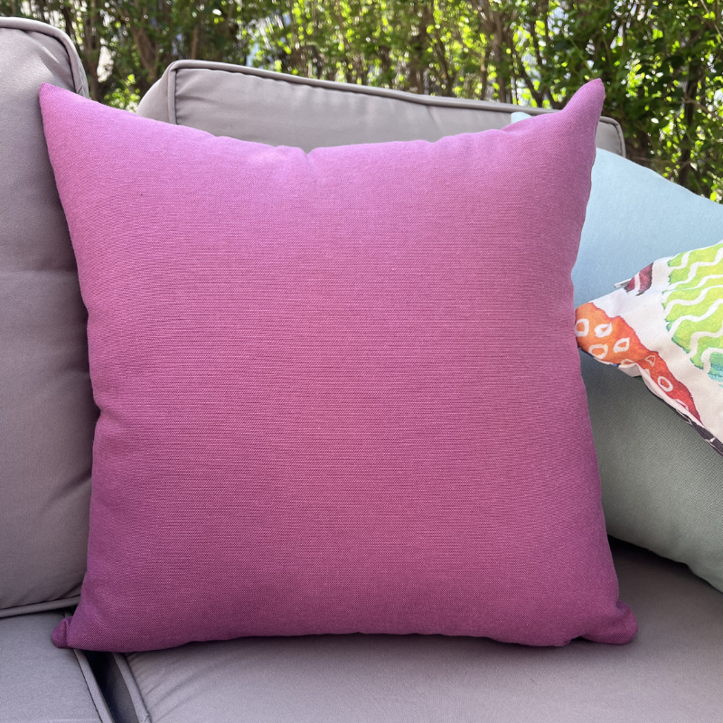 Purple cushion cover displayed on a beige outdoor sofa in a garden patio setting