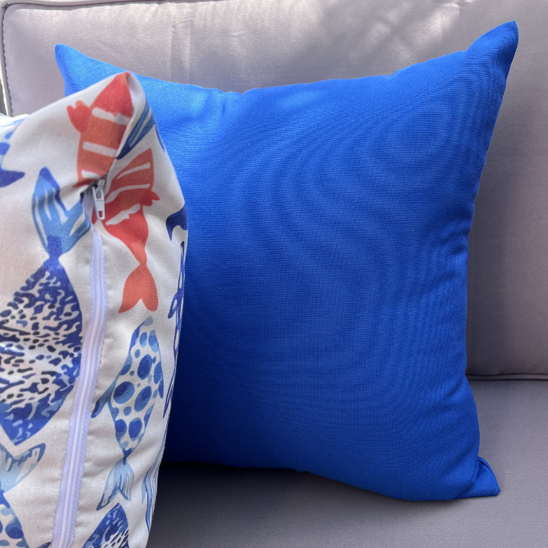 Royal blue cushion cover displayed on a beige outdoor sofa in a garden patio setting