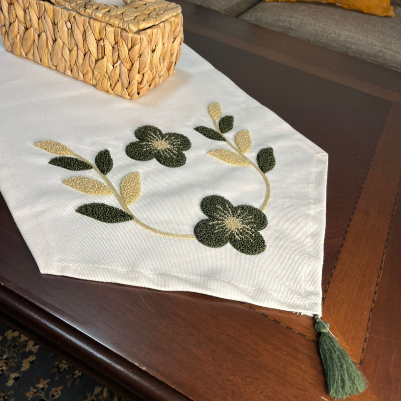 White embroidered table runner with green and gold floral design on wooden coffee table