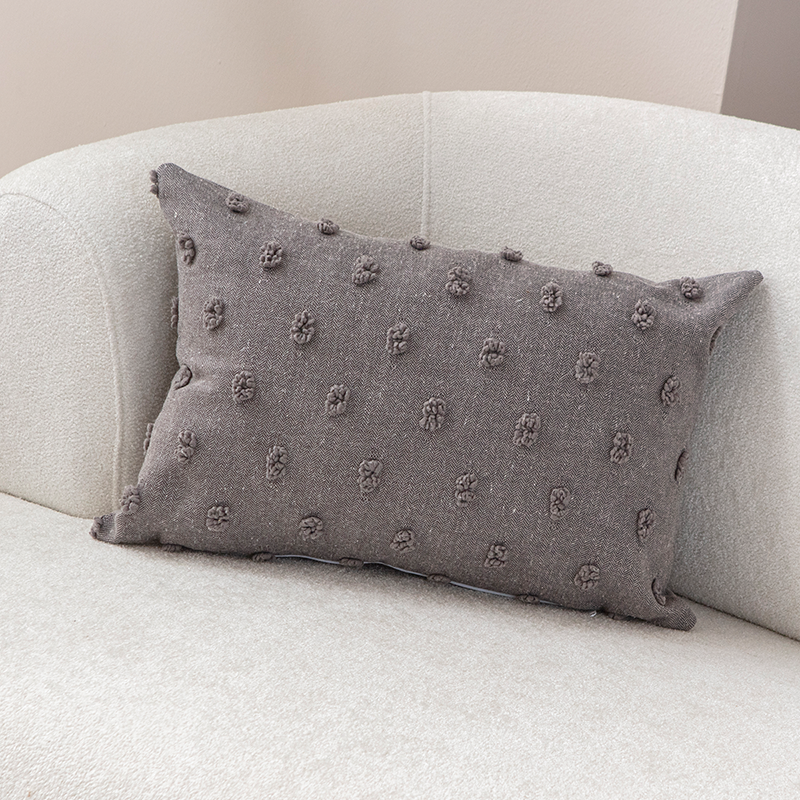 Taupe textured cushion with raised knot-dot details placed on a light beige curved sofa.